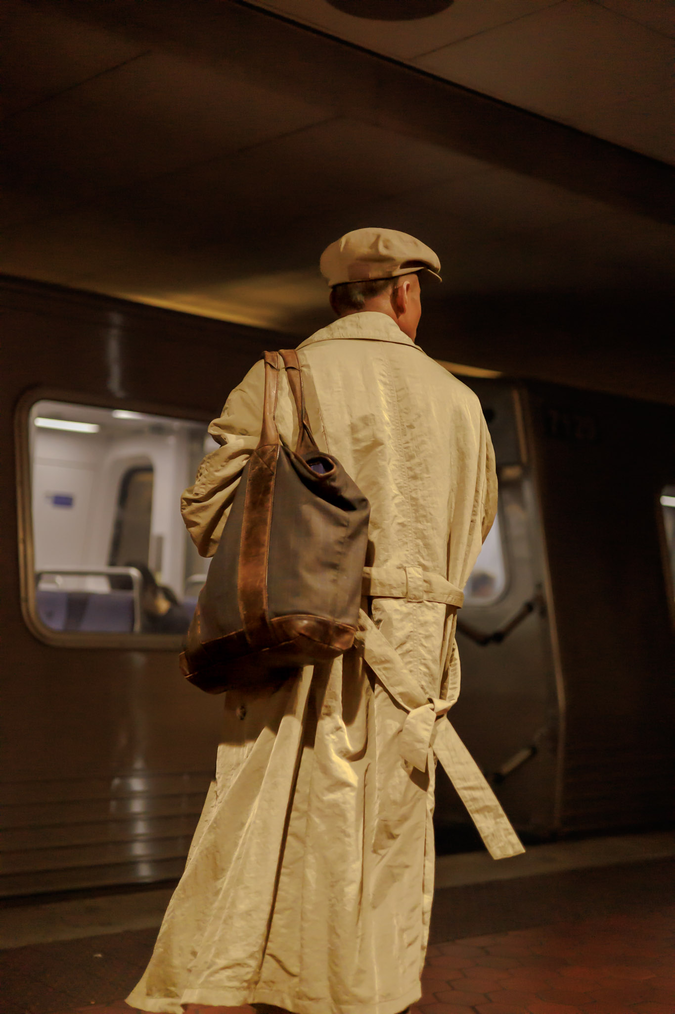 a man in a powerful overcoat and cap looks over at his arriving metro train in Washington, D.C.