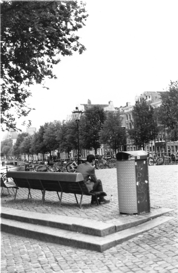 A man sitting alone on a bench beside an Amsterdam canal