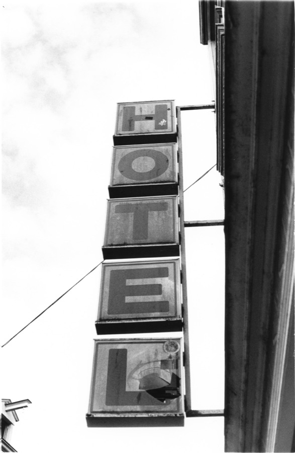 A hotel sign, its five weathered letter panels unlit against a white sky