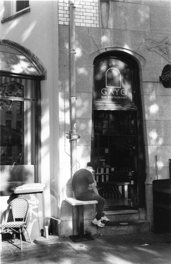 A man bent over his phone on a stool outside a shuttered bar