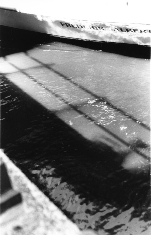 Sunlight and railing shadows across dark canal water beside a moored boat