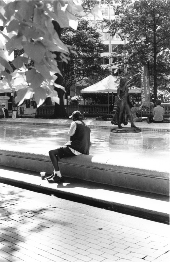 A man sitting at the edge of a fountain, a bronze figure mid-stride behind him