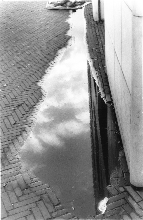 A puddle on brick paving holding the reflection of clouds
