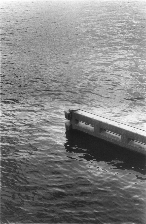 A low concrete jetty reaching out into open, wind-textured water