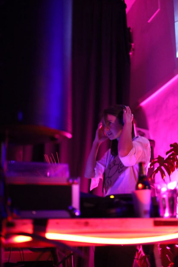 A DJ adjusting her headphones under magenta stage light