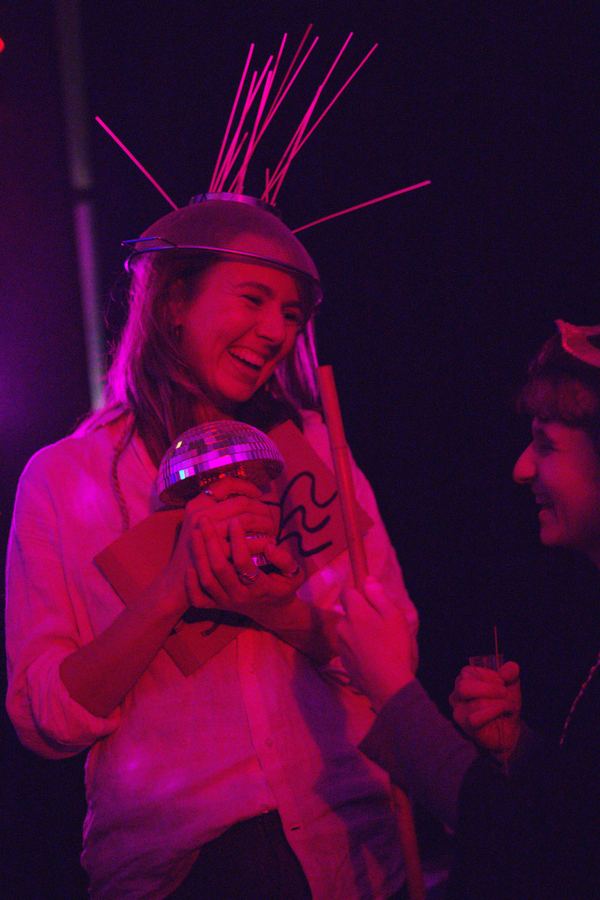 A guest in a glow-stick headdress laughing as she holds a disco-ball trophy