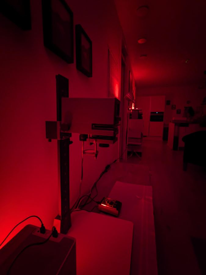 A photographic enlarger on a darkroom bench, lit only by red safelight
